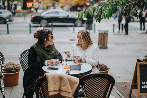 Obraz na plátne Two friends share a conversation while having coffee at a cozy outdoor cafe in the city