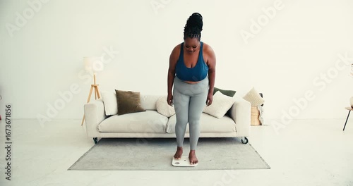 Overweight black woman in sportswear uses smart scale near sofa