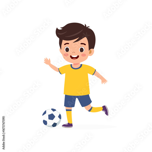 Happy young boy in yellow shirt and blue shorts plays soccer kicking a ball forward