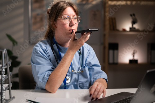 Fotografija physician nurse using smartphone dictate voice message working over hours in hospital office on night shift