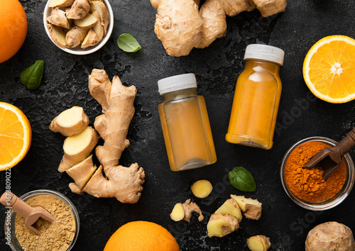 Bottles of immune ginger and orange energy shot drink with ginger root and turmeric powder on black background.Top view.