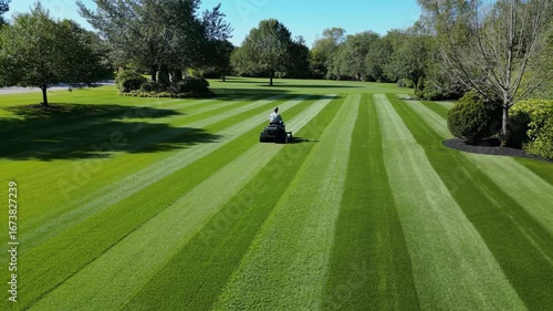 A person on a riding lawn mower creates perfect stripes on a huge green lawn this meticulous landscaping shows order precision professional care a beautiful maintained property