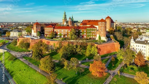 Krakow, Poland. State owned royal Wawel Castle and Gothic Cathedral, park, boulevards, promenades with walking people and bikers. Aerial 4K approaching video in autumn in sunset light