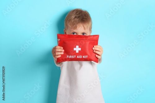 Child holds a bright red first aid kit against a light blue background 