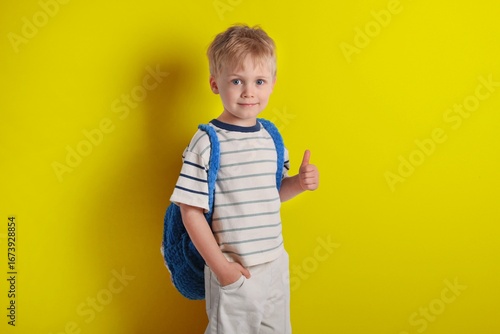 Boy giving thumbs up with blue backpack in front of bright yellow background