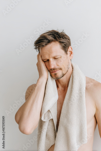 calm man wipes his face with towel exhaling deeply eyes closed relaxing after refreshing shower