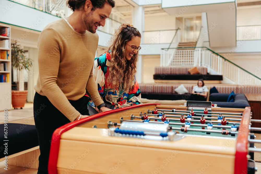 Fototapeta premium Coworkers enjoying a fun and relaxing lunch break playing foosball in a modern office