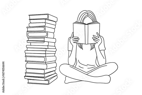 Young woman sitting cross legged reading a book next to a tall stack of books