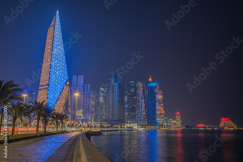 Doha city business downtown center panorama illuminated at night, with modern skyscrapers and sea in the foreground, Qatar