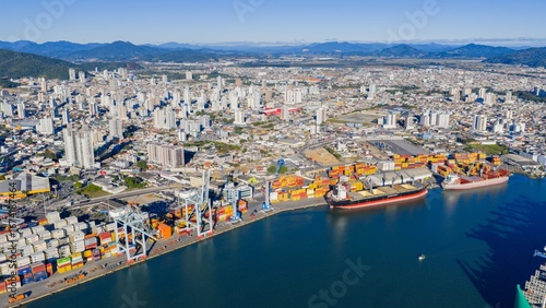 Aerial panoramic view of the Port of Itajaí with container ships and city skyline in the background.