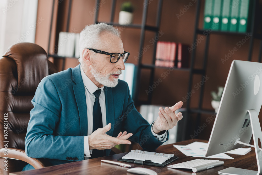 Fototapeta premium Senior businessman working attentively on a computer in an office setting wearing a blue suit