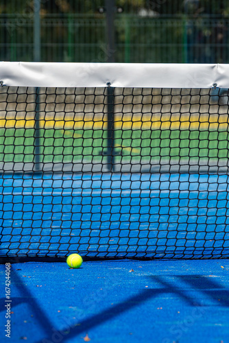 Yellow paddle tennis ball lying on blue turf near net