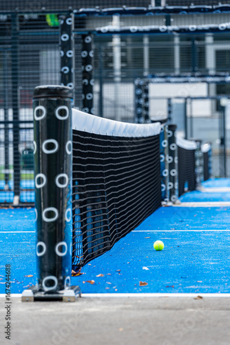 Yellow paddle tennis ball lying on blue paddle court near net