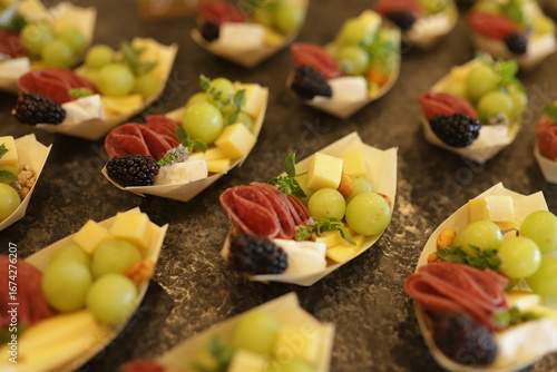Appetizing close-up of small individual charcuterie cups with grapes, cheese cubes, cured meats, and blackberries. Perfect for food, catering, and lifestyle concepts.