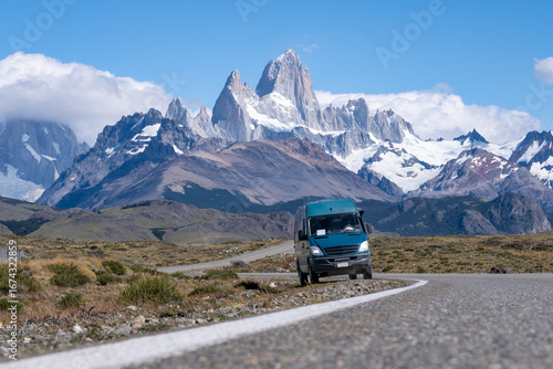 A camper van navigates a scenic winding road with the magnificent Mount Fitz Roy towering under a clear blue Patagonian sky, an invitation to adventure
