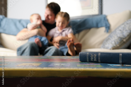 Bible on Table with Father and Children on Couch in Background