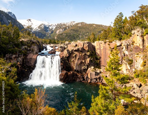 Fototapeta Naklejka Na Ścianę i Meble -  Scenic waterfall cascading into a rocky pool, surrounded by lush greenery and mountains