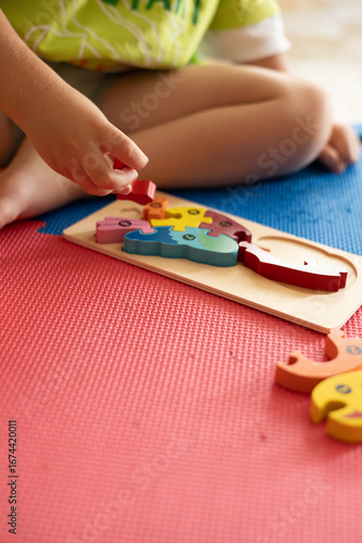 Child engaged in playful learning with colorful wooden puzzle on bright rubber mat in a well-lit room during daytime