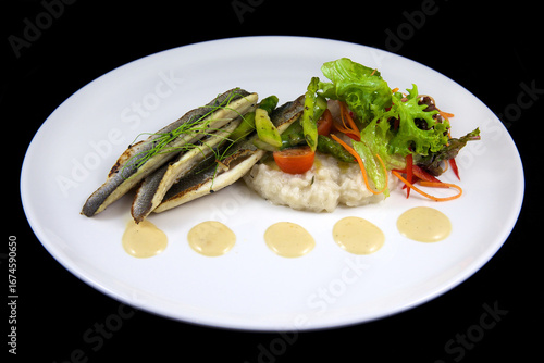 Appetizing restaurant dish. Grilled fish with rice and fresh herbs on a white plate. On a black background. Haute cuisine.