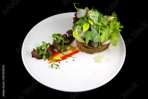 Beautiful haute cuisine restaurant dish. Fried pieces of meat with sauce, fresh herbs and crispy bread. On a white plate, on a black background.
Restaurant food. Chef's dish.