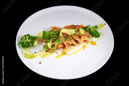 An exquisite dish of fresh red fish, with avocado slices, decorated with greens. On a white plate, with a beautiful presentation. Chef's menu. Restaurant dish. On a black background.