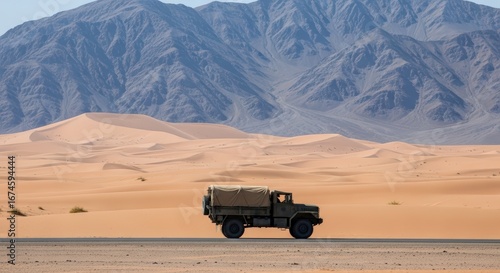 Military Style Truck Driving on a Remote Desert Highway with Sand Dunes and Mountains