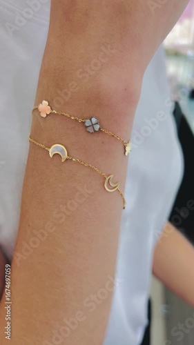 Young woman wearing a simple white t-shirt showcases delicate gold bracelets with mother of pearl on her wrist, highlighting elegant jewelry in a bright retail environment