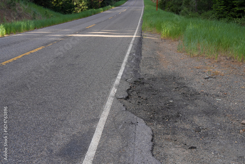 Large pothole disrupts a paved road, highlighting the need for maintenance and repair.  Green grass and road ahead visible at top of frame.