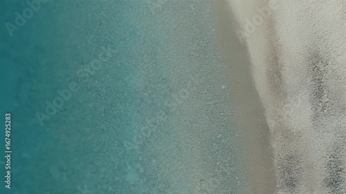 Aerial view of a sandy beach meeting the turquoise ocean water, showing the shoreline and the transition between sand and sea.