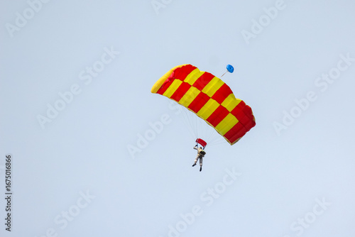 Skydiver descends with colorful parachute over open sky during bright daylight