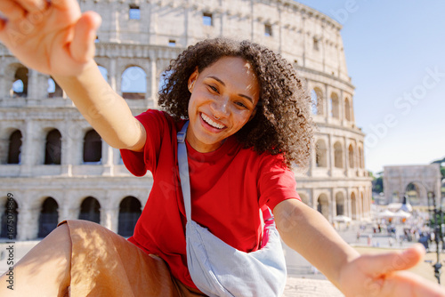 A joyful young woman poses with arms outstretched in front of the historic Colosseum in Rome, embodying the essence of travel, adventure, and happiness during her city exploration