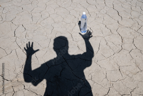 Photography Male shadow reaches hands into bottle of drinking water against heat cracked cla