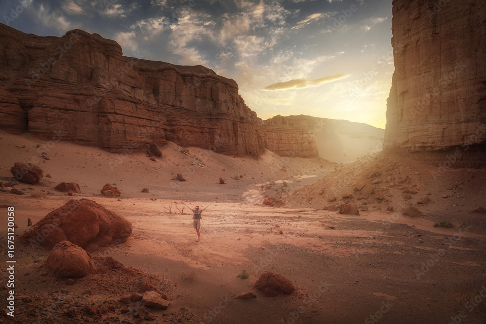 Fototapeta premium A traveler in a serene desert canyon at sunset, with mountains and sky