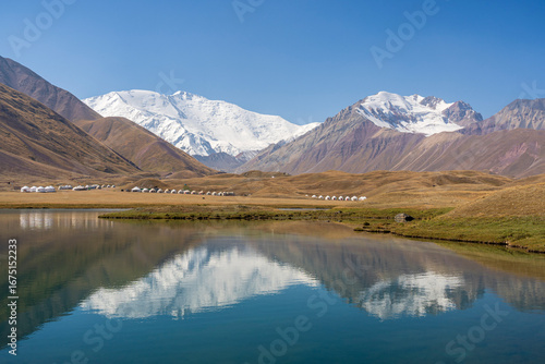 Landscape view of Lenin Peak aka Ibn Sina peak in Trans Alay mountain range with reflection in Tulpar Kul lake and yurt camp, Sary Mogul, Kyrgyzstan