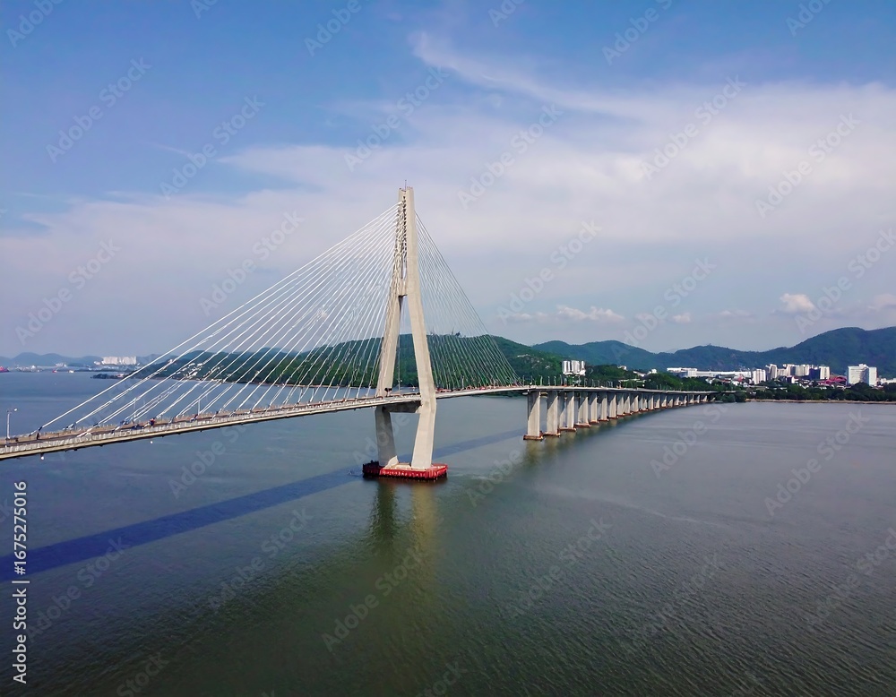 Fototapeta premium Modern Cable-Stayed Bridge Spanning a Wide Body of Water with Distant Cityscape.