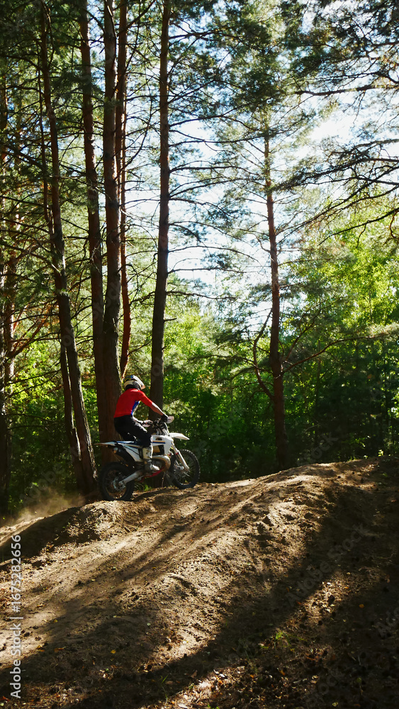 Fototapeta premium A motorcyclist in a red shirt rides a dirt bike through a sunny forest
