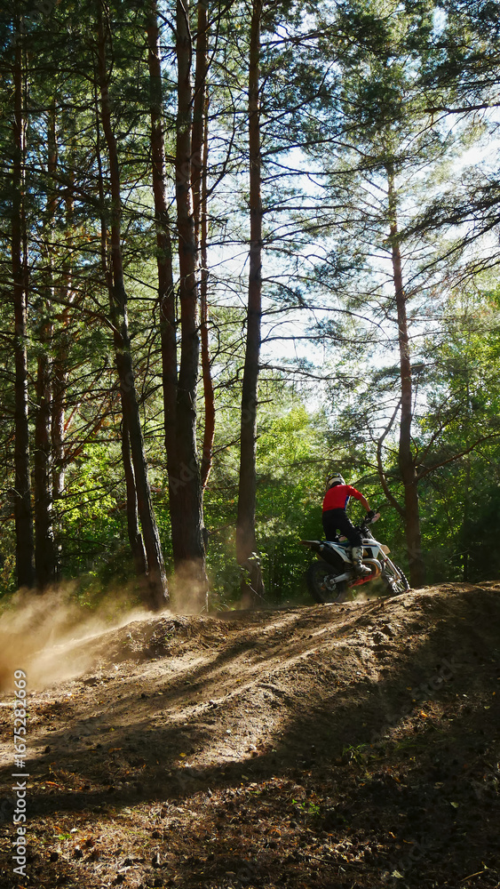 Fototapeta premium A enduro man jumps a dirt bike in a forest, soaring through the air