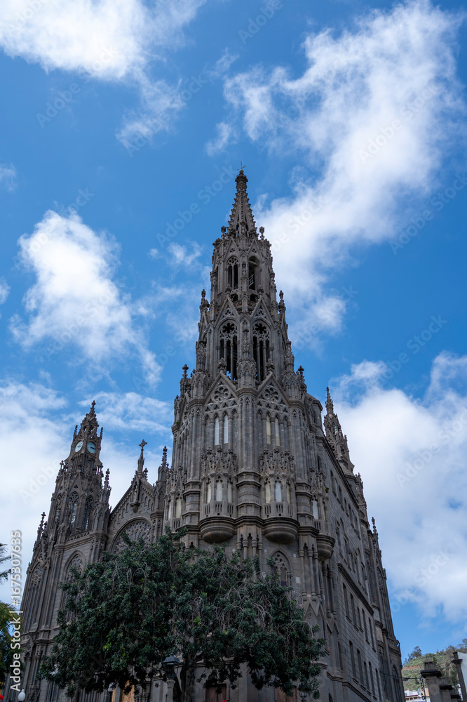Fototapeta premium A tall building with a steeple and a clock tower. The sky is blue and there are clouds in the background