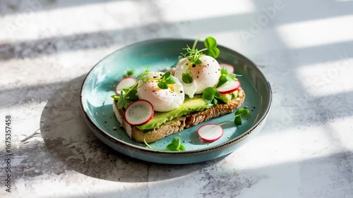 Fototapeta Modern minimal food styling shot of avocado toast poached eggs radish slices microgreens arranged neatly on a ceramic plate The plate sits on a light concrete surface with soft natural side lighting