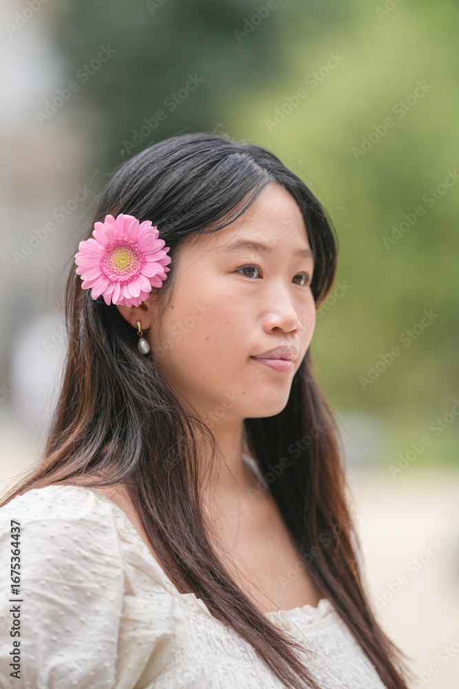 A woman with long brown hair and a pink flower in her hair. She is wearing a white shirt and a pearl earring A woman with long brown hair and a pink flower in her hair. She is wearing a white shirt and a pearl earring