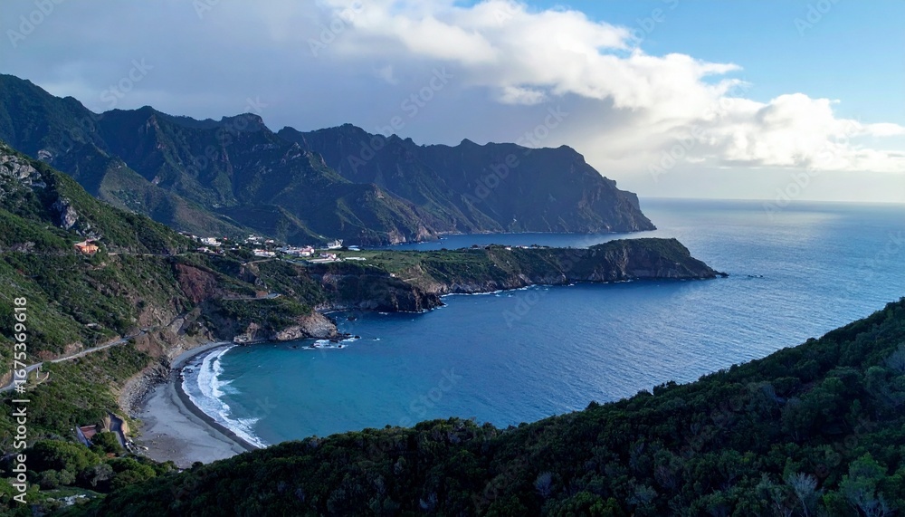 Fototapeta premium Aerial view of a scenic coastal landscape featuring a serene bay, mountains, and the vast ocean under a cloudy sky.