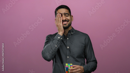 Foto Young man holding cube smiling over pink background, wearing glasses and black shirt, expressing happiness and contemplation