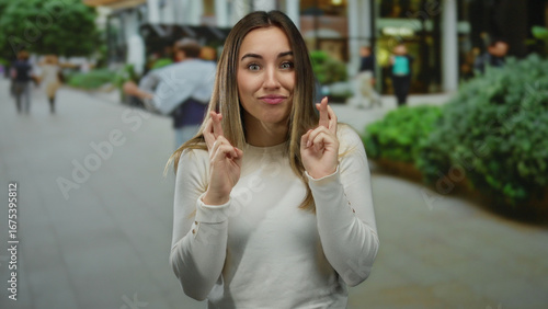 Woman outdoors with fingers crossed showing hopeful expression on a bustling city street, embodying anticipation and wishful thinking in a vibrant urban setting.