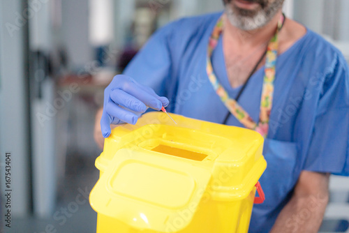 Fototapeta Doctor disposing of needle in sharps container: safe medical waste disposal