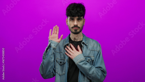Fotografía Young hispanic man making a gesture with hand over heart against isolated pink background, expressing sincerity and promise with calm demeanor