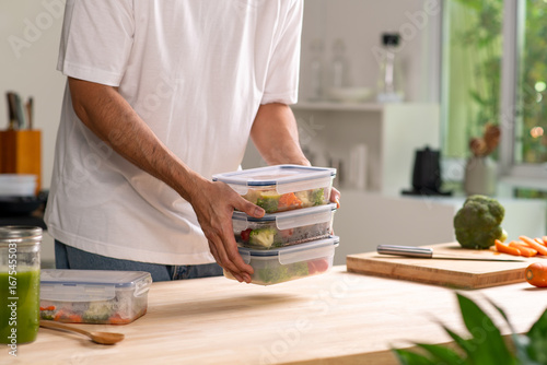 Man preparing healthy homemade meal prep in food container with fresh food at home.