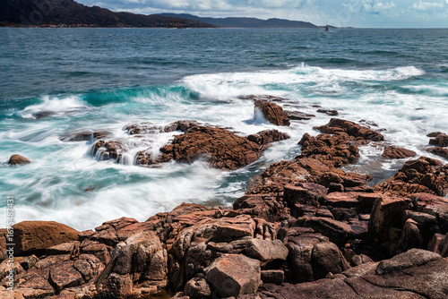 Schilderij op canvas Turquoise waves crashing on orange rocks in Cee Galicia