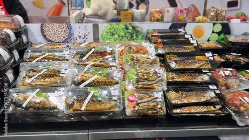 Close view of assorted cooked fish packaged in plastic trays at a retail grocery counter.