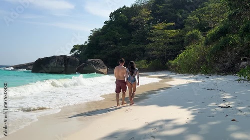 Couple walking hand in hand along tropical sandy beach with turquoise water at Similan Islands, Thailand.