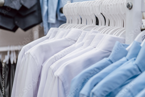 neatly arranged dress shirts hang from hangers in clothing retail store, featuring various light colors for children. school uniform simple and comfortable. sale. close up.